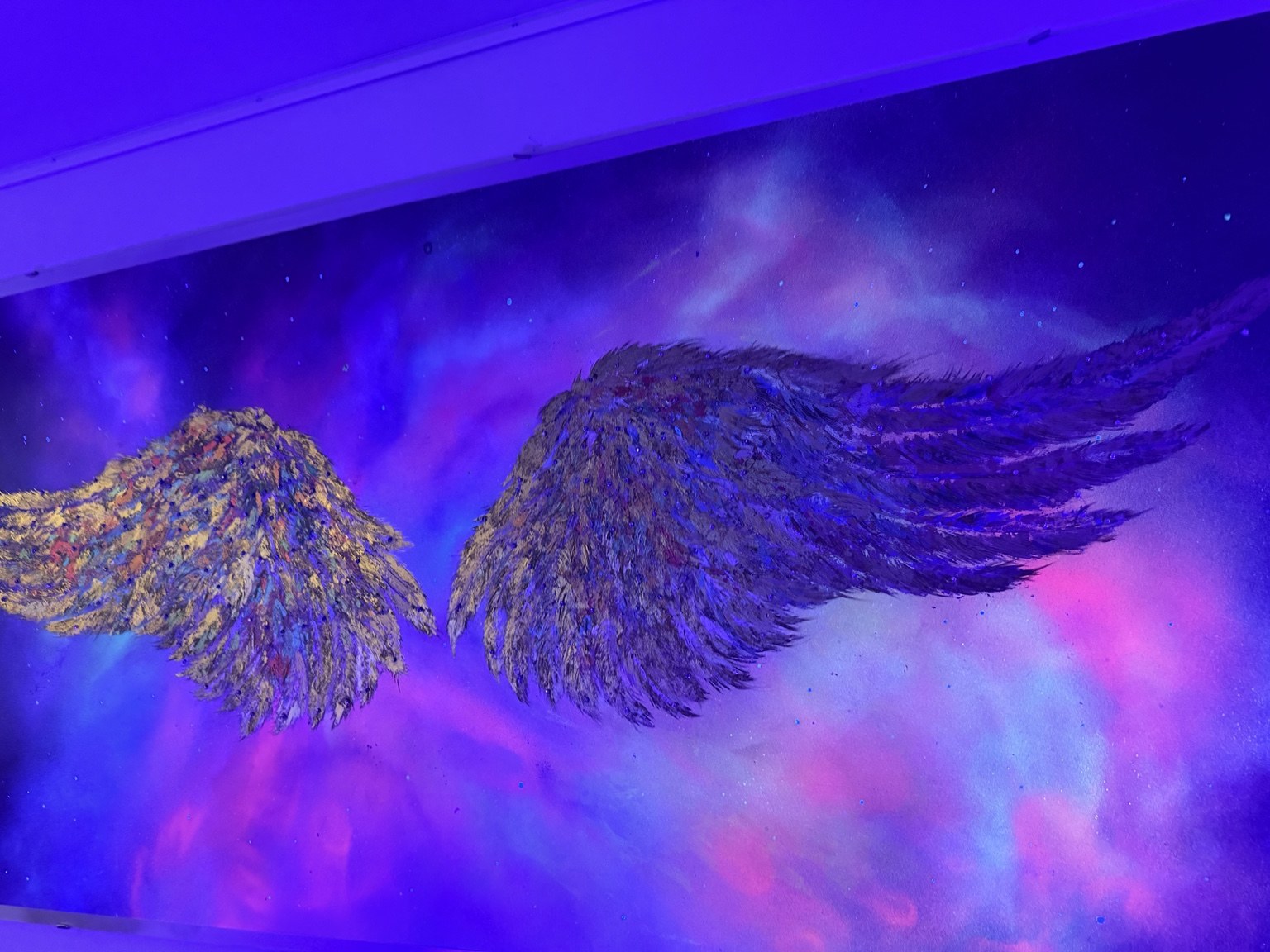 Sculpted angel wings in gold against a glowing blue and violet celestial background