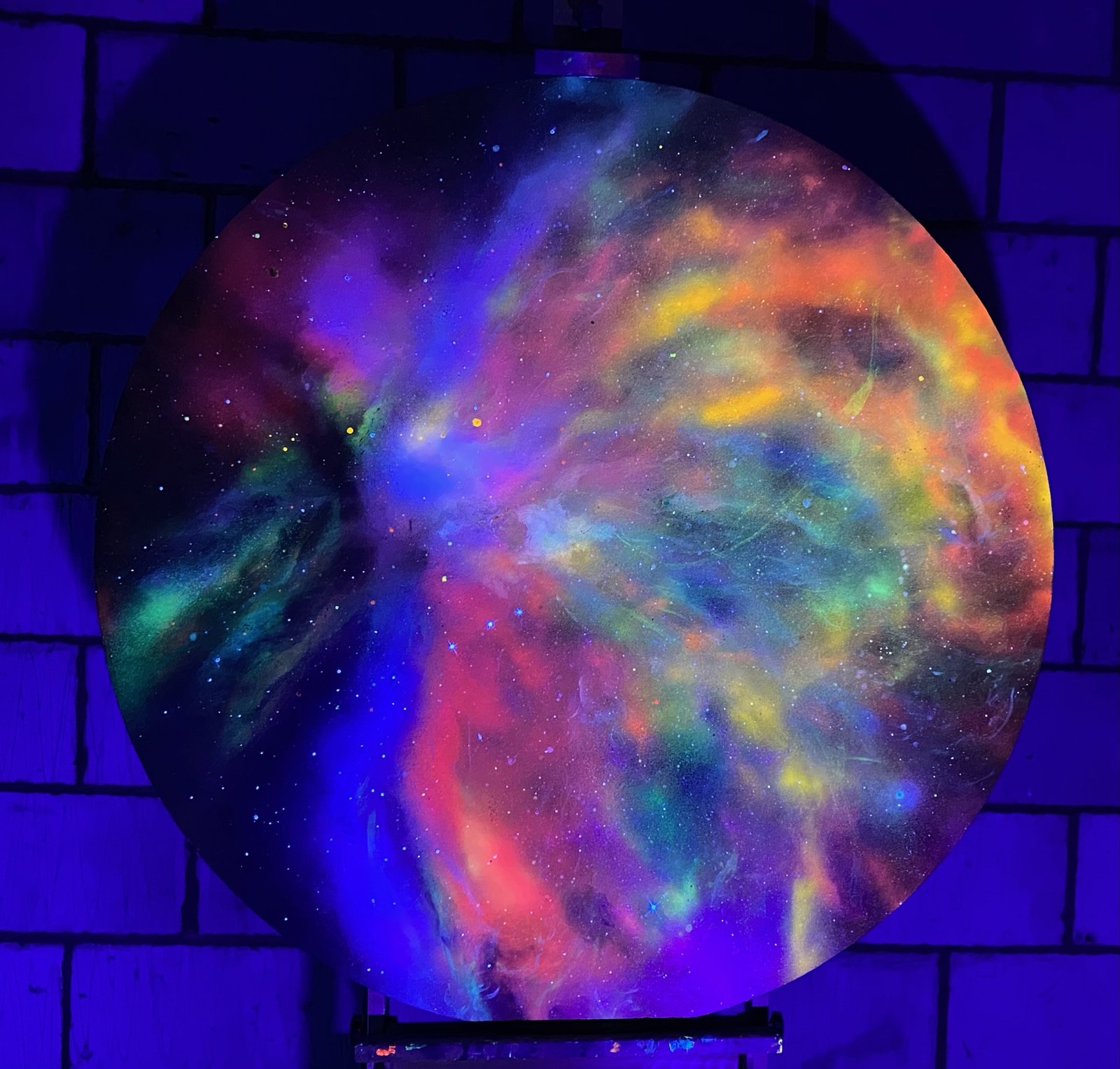 Circular celestial artwork glowing with blue, violet, orange and green clouds of colour