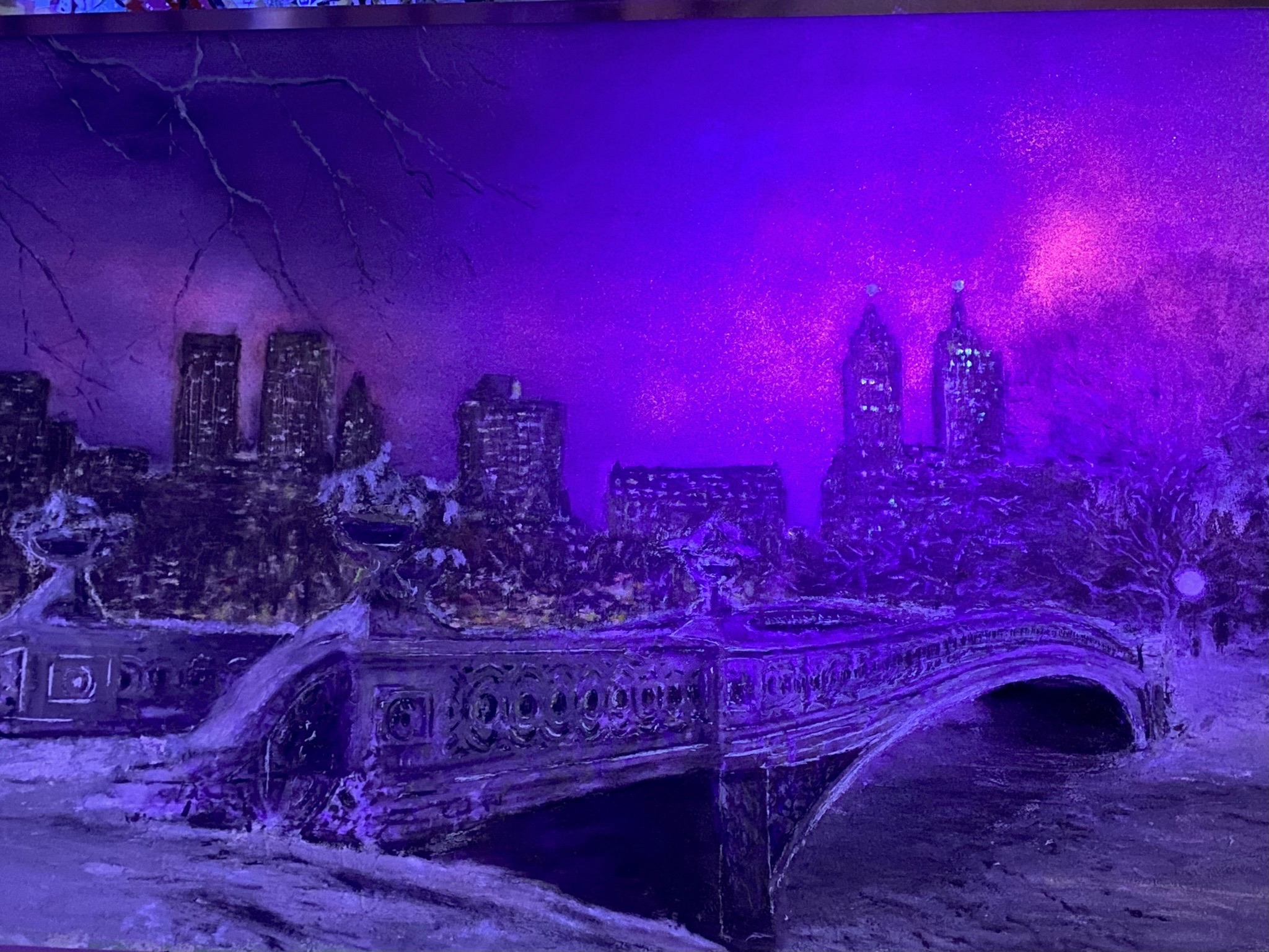 Winter Wonderland NYC artwork illuminated in vivid purple UV light, with snowy Bow Bridge and the Manhattan skyline